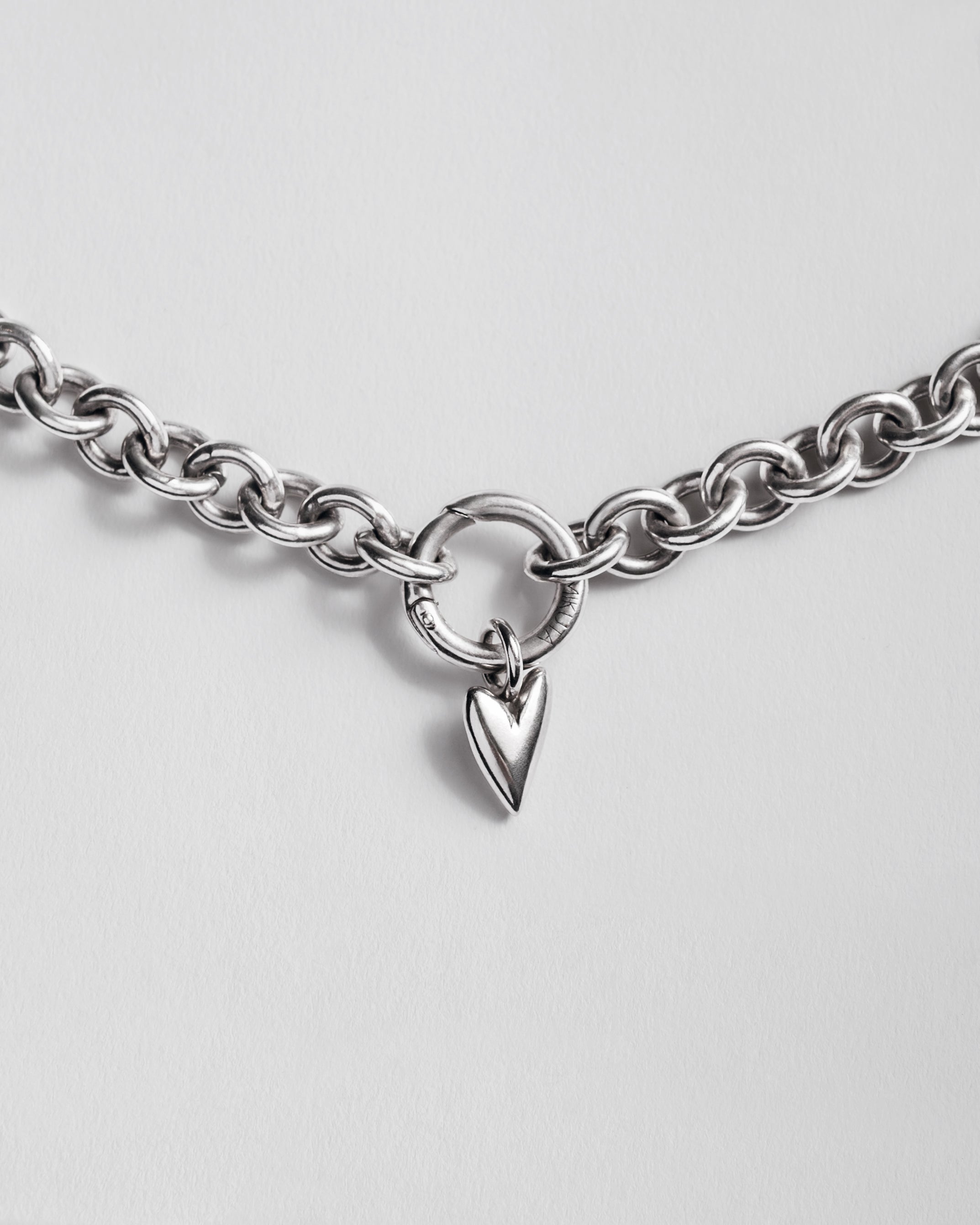 Silver chain necklace with a heart-shaped pendant on a light gray background