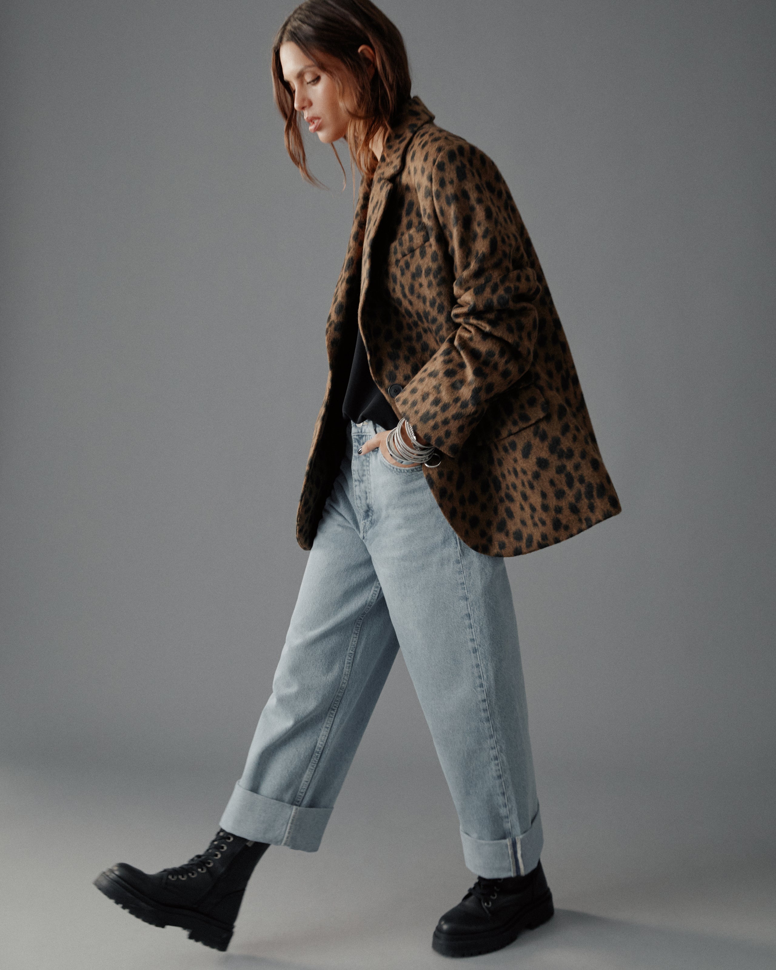 Person wearing a leopard print coat, light blue jeans, and black shoes on a gray background