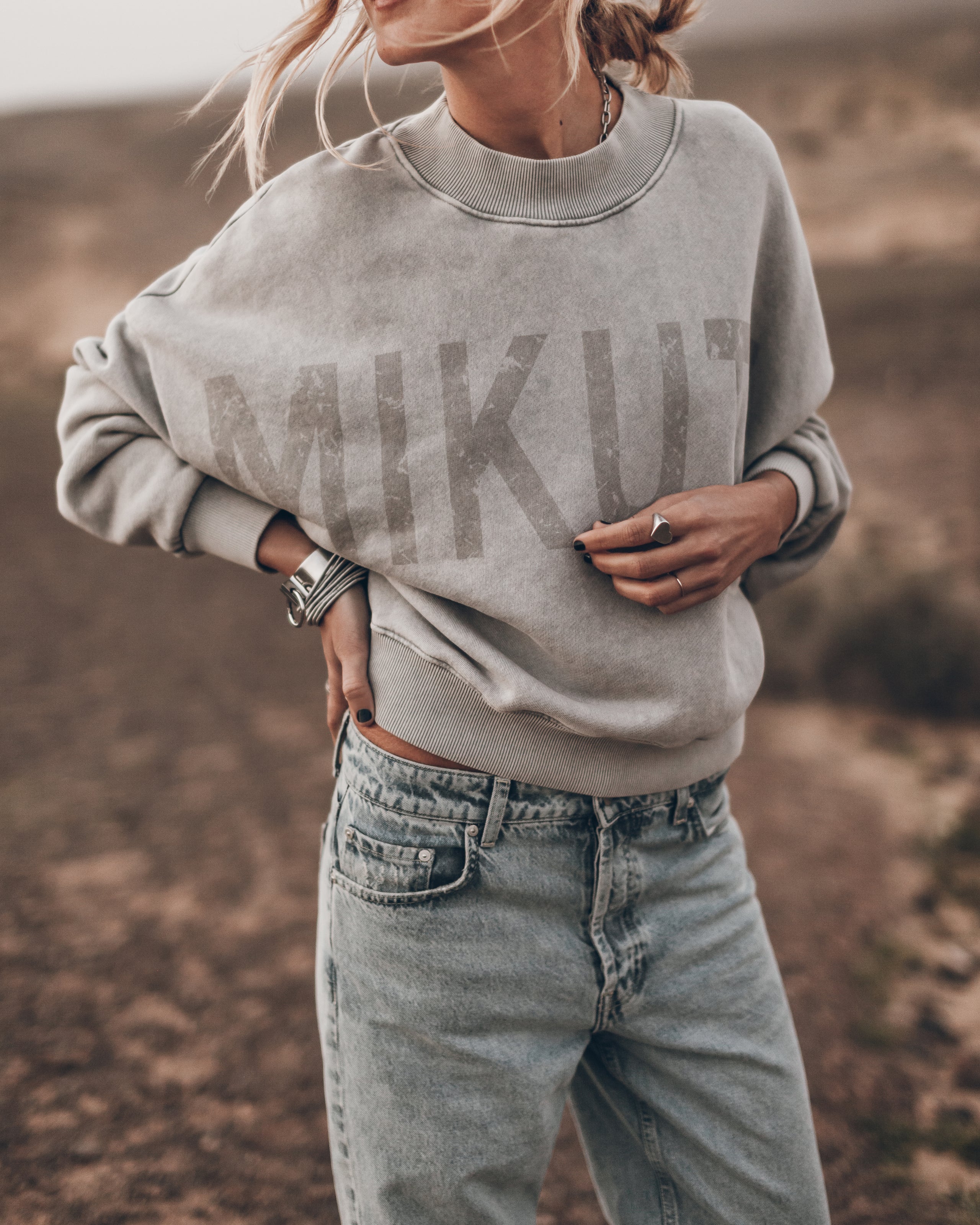 Person wearing a gray sweatshirt with 'MIKU' branding in a desert-like setting
