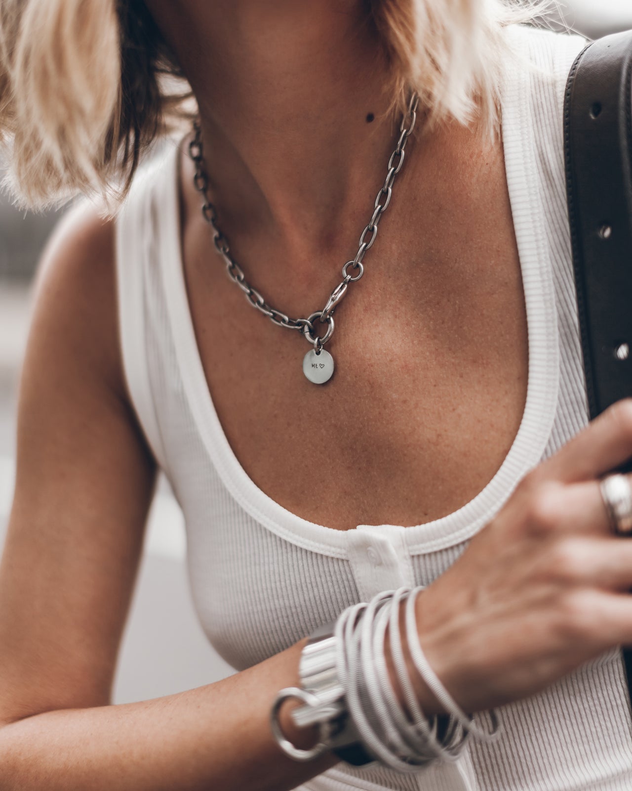 Person wearing a white tank top and silver necklace with heart pendant.