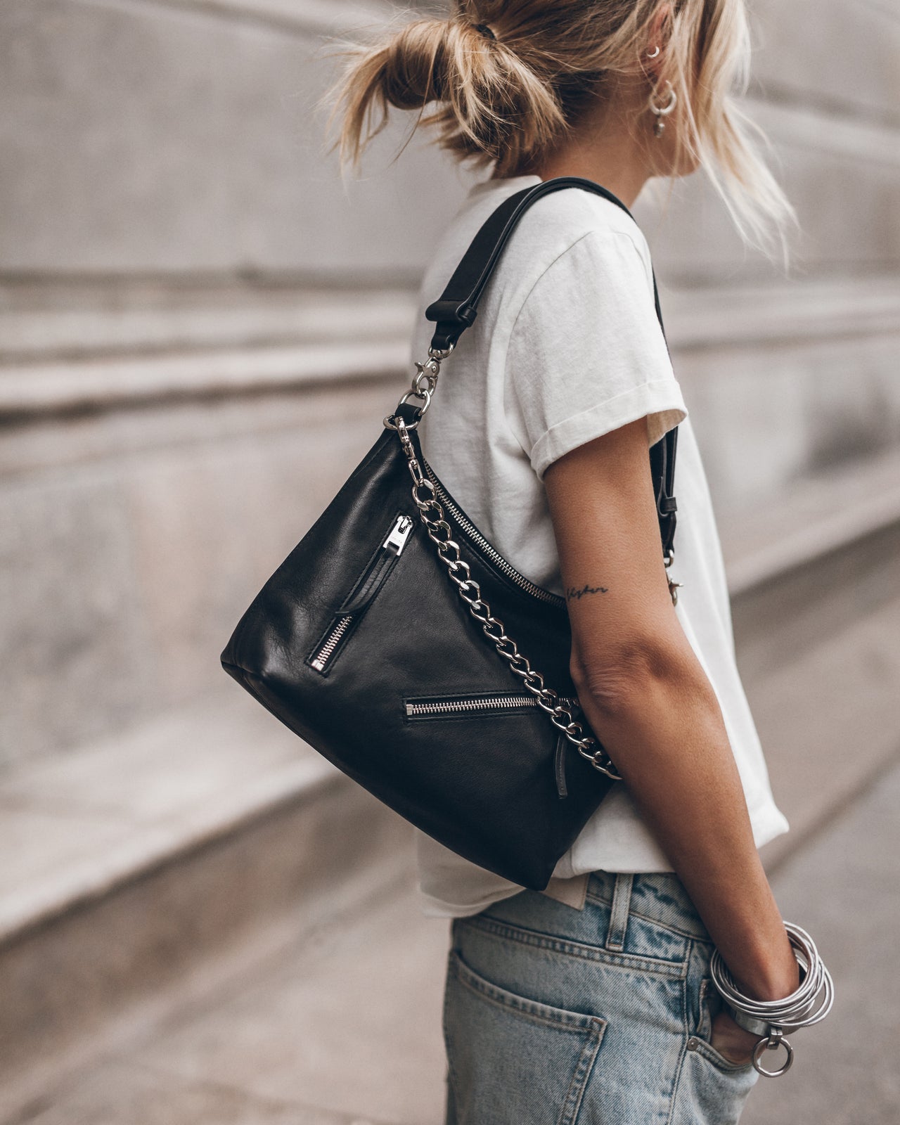 Woman  holding a black handbag with a chain detail, wearing a white t-shirt and blue jeans.