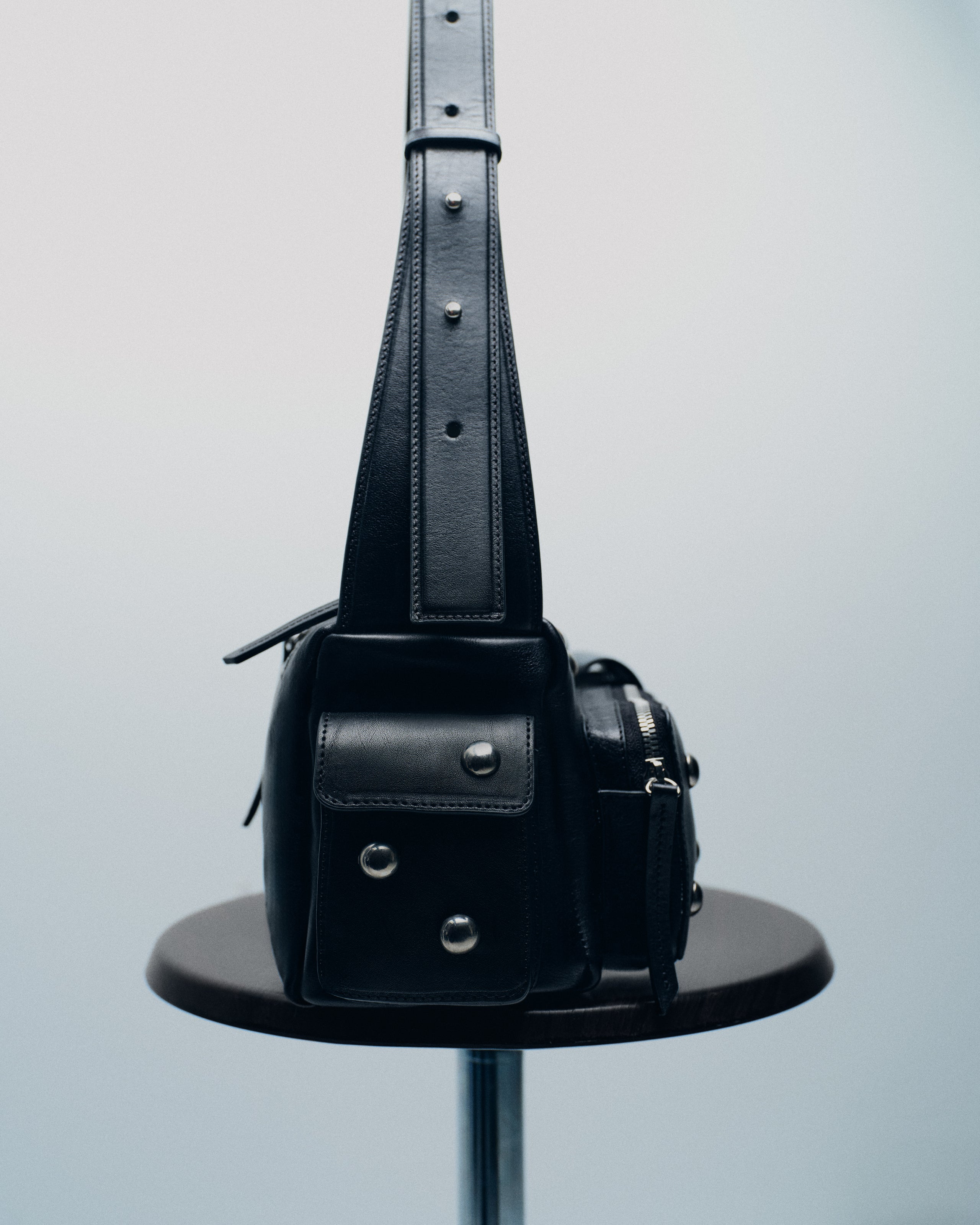 Black leather crossbody bag with silver hardware on a stool.
