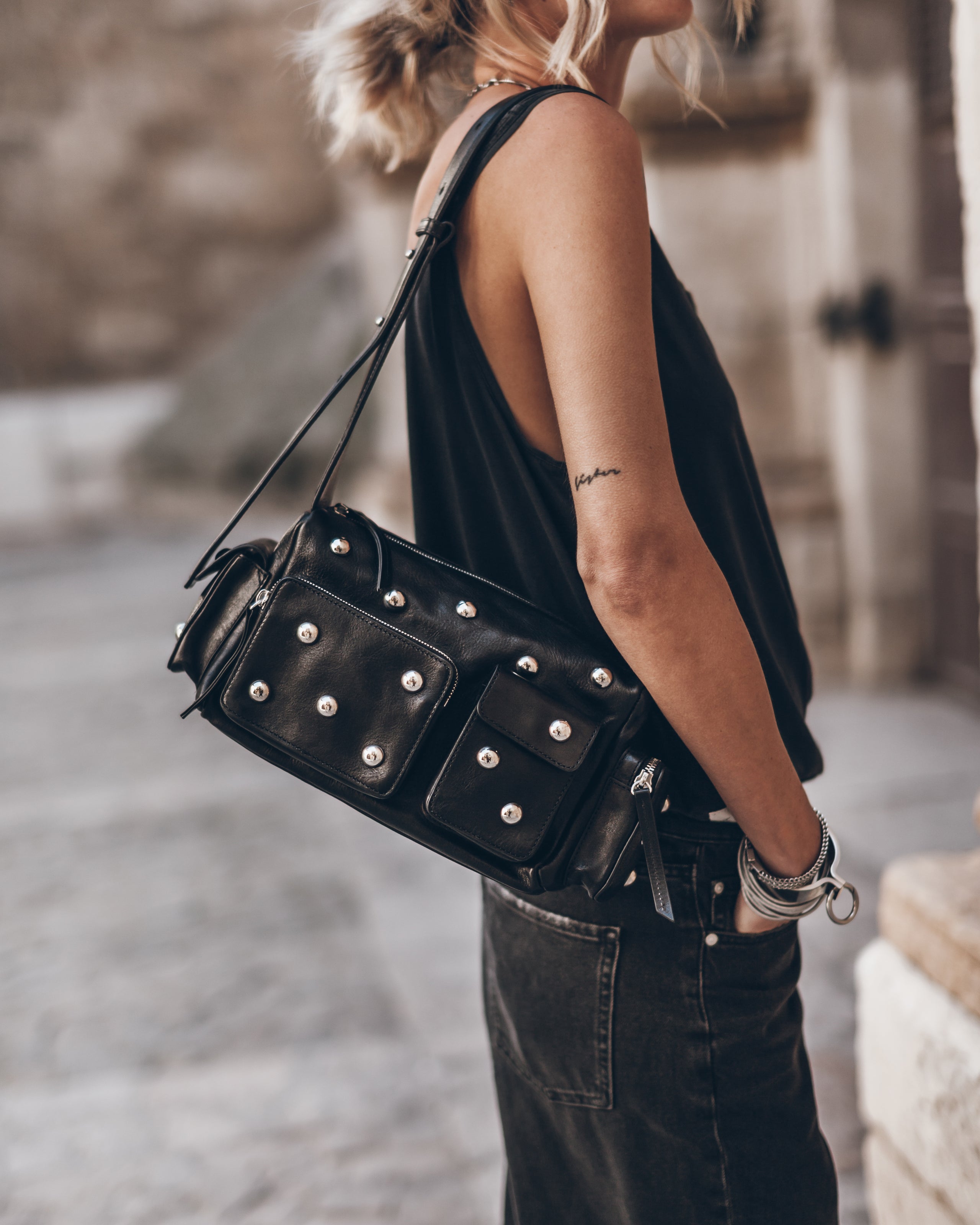 Woman wearing black tank top and jeans, with a studded black leather shoulder bag.