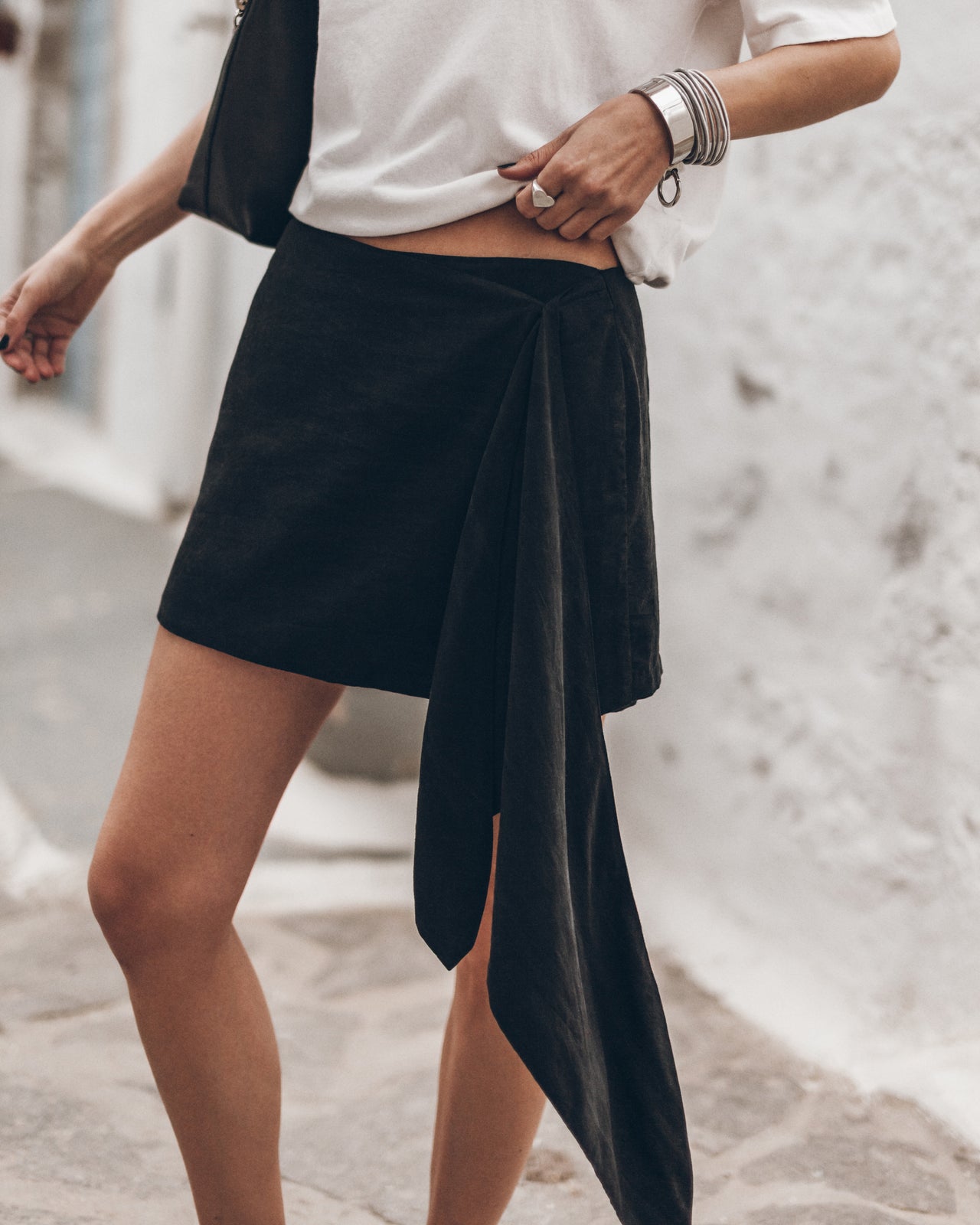 Woman wearing a black wrap skirt with a white t-shirt against a light background.