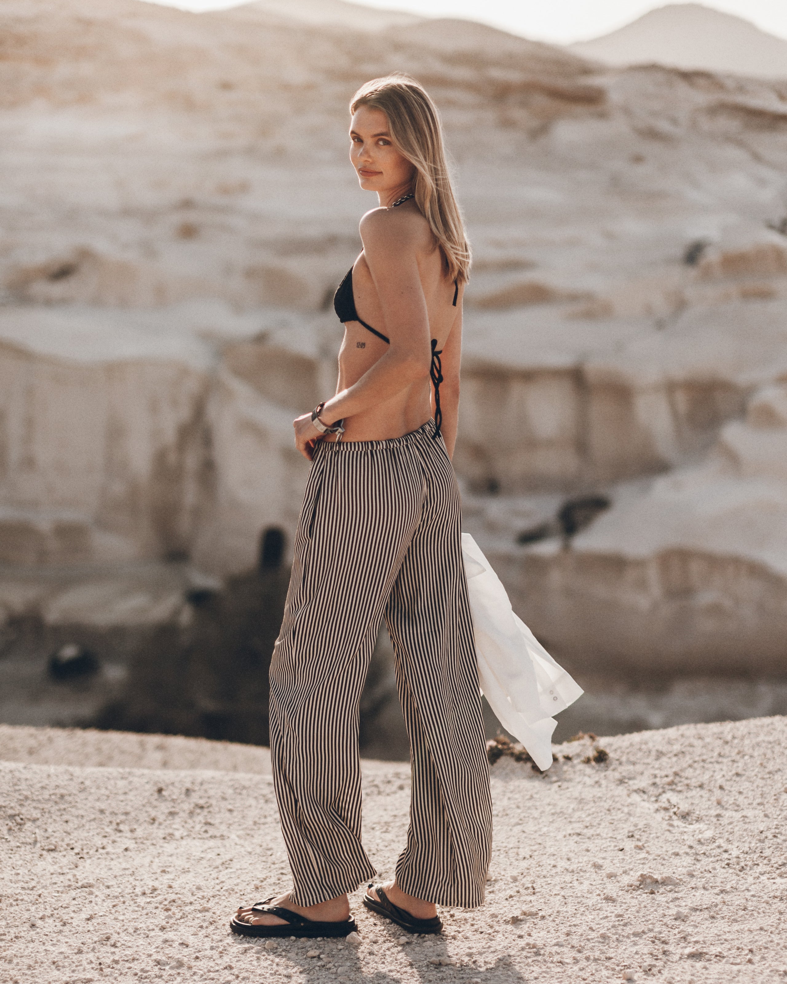 Woman in a black bikini top and striped pants standing in a desert landscape.