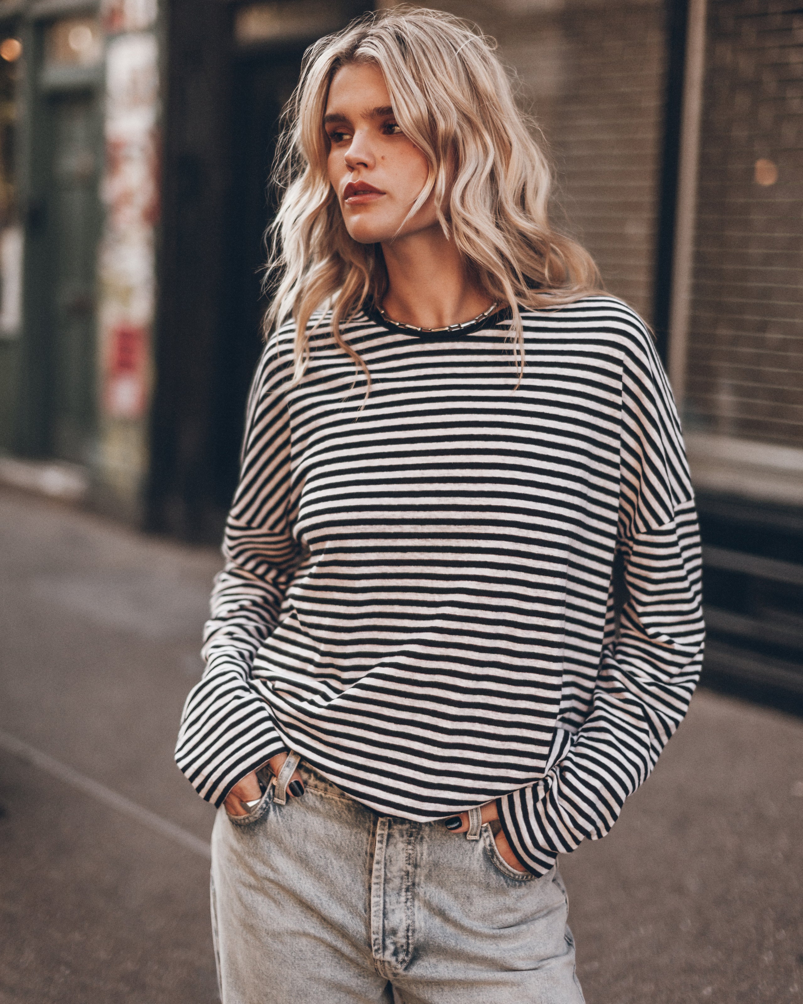 A woman wearing a black and white horizontally striped longsleeve  top with light-wash jeans, standing on an outdoor city street.