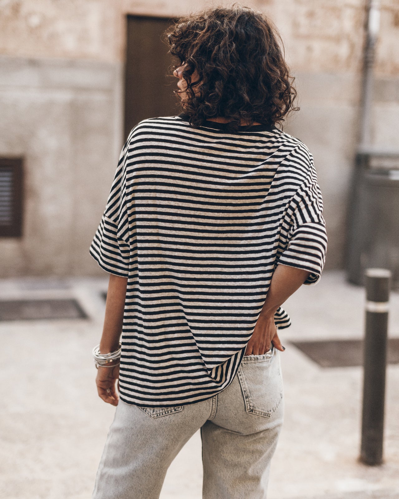 Woman wearing a striped t-shirt and light jeans standing on a street.