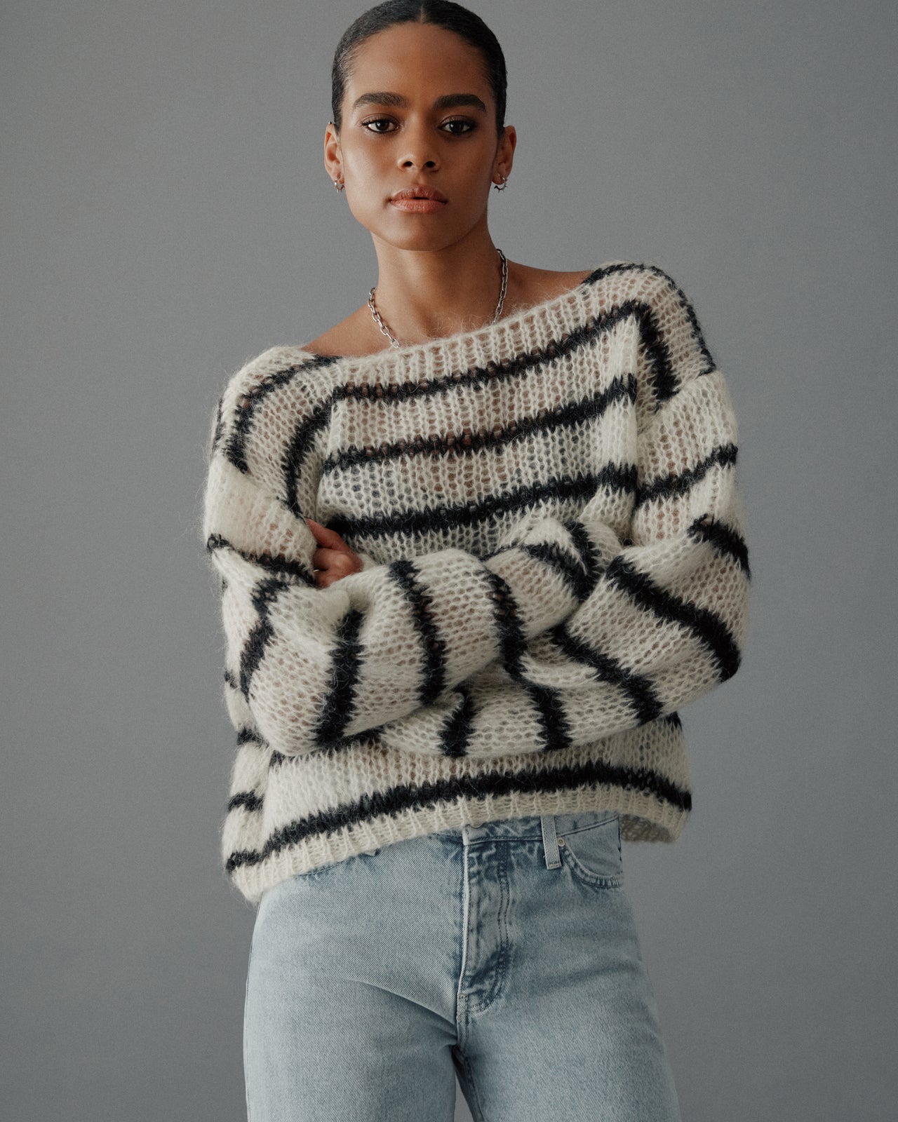 Person wearing a black and white striped sweater with light blue jeans against a gray background