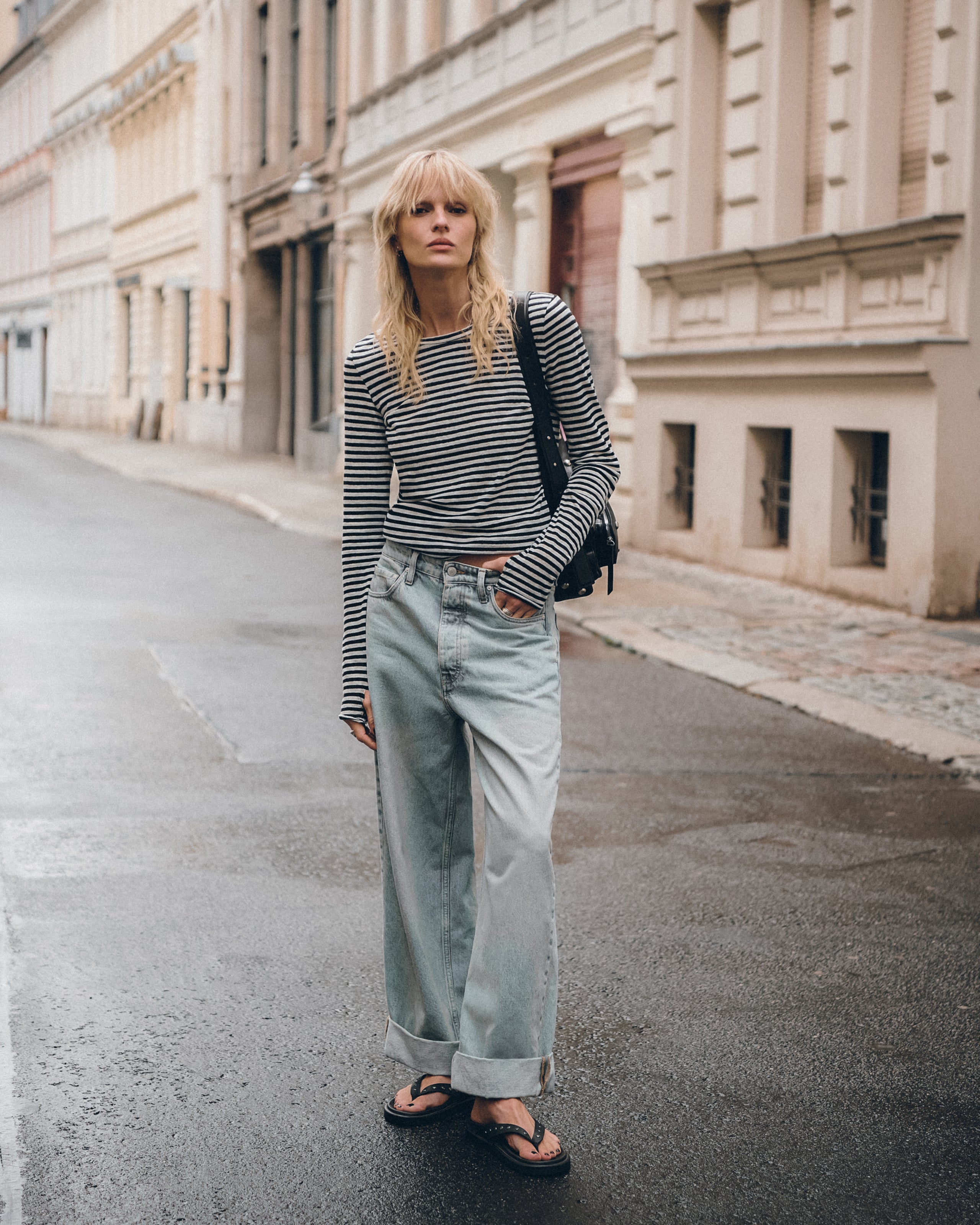Person wearing a striped sweater and light blue jeans standing on a street.