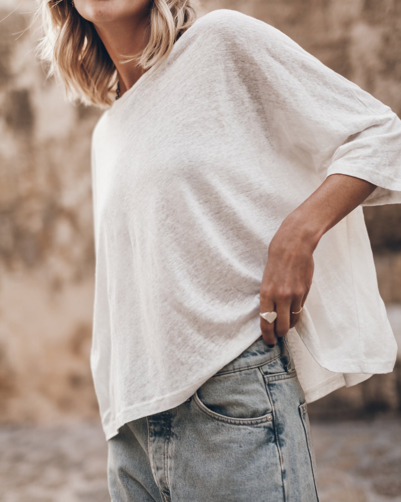 White loose linen T-shirt with relaxed fit and three-quarter sleeves worn untucked over jeans.