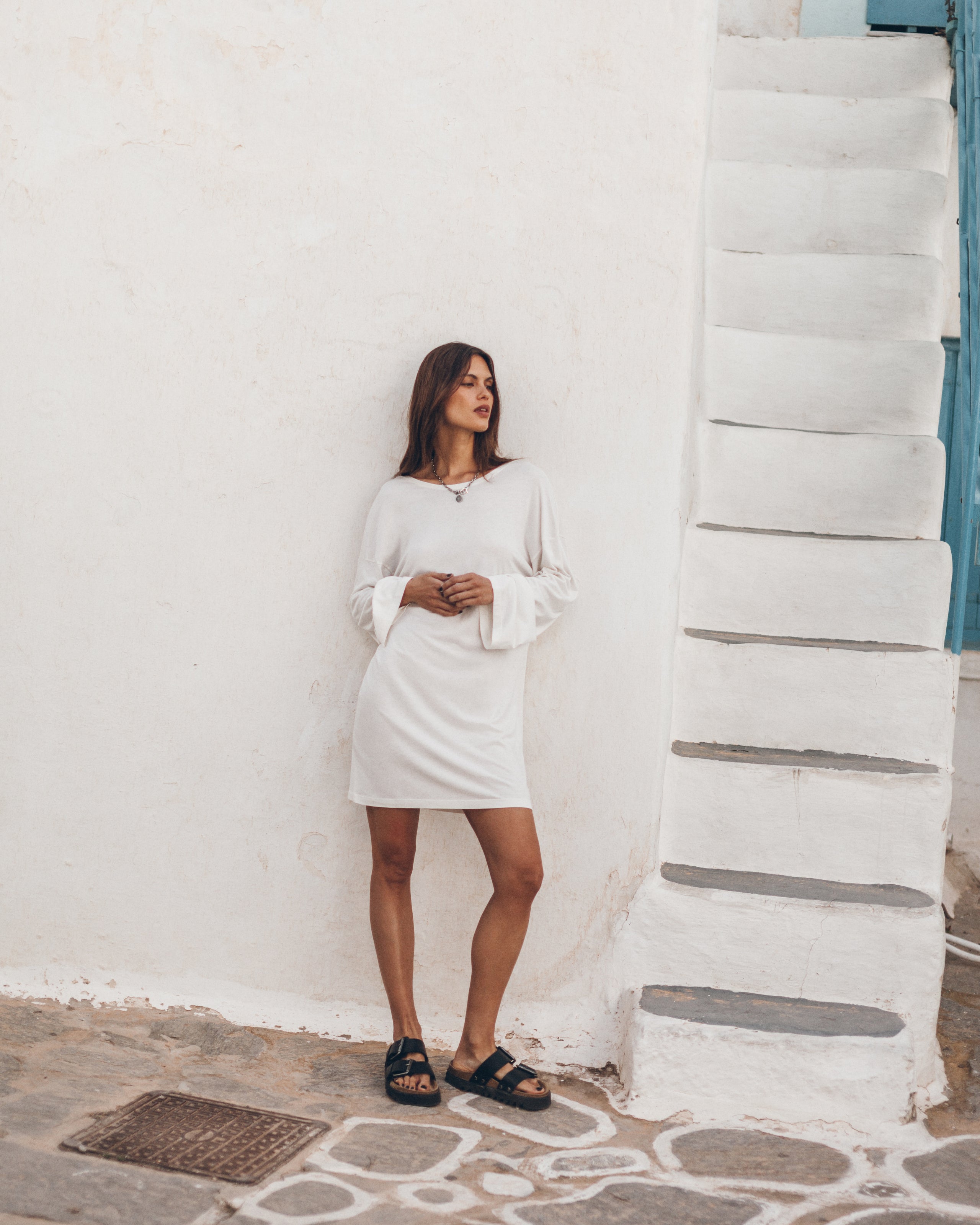 Woman in a white dress standing against a white wall.