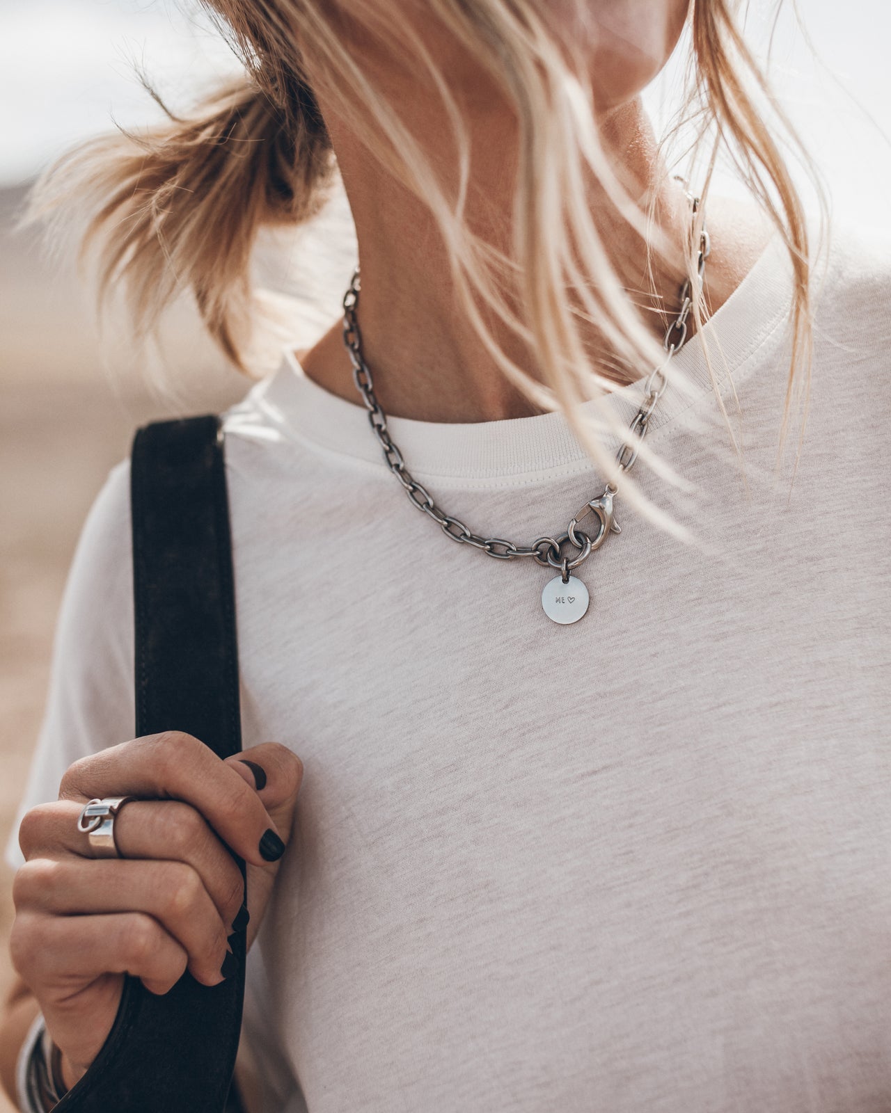 Person wearing a white shirt with a necklace and holding a black bag.