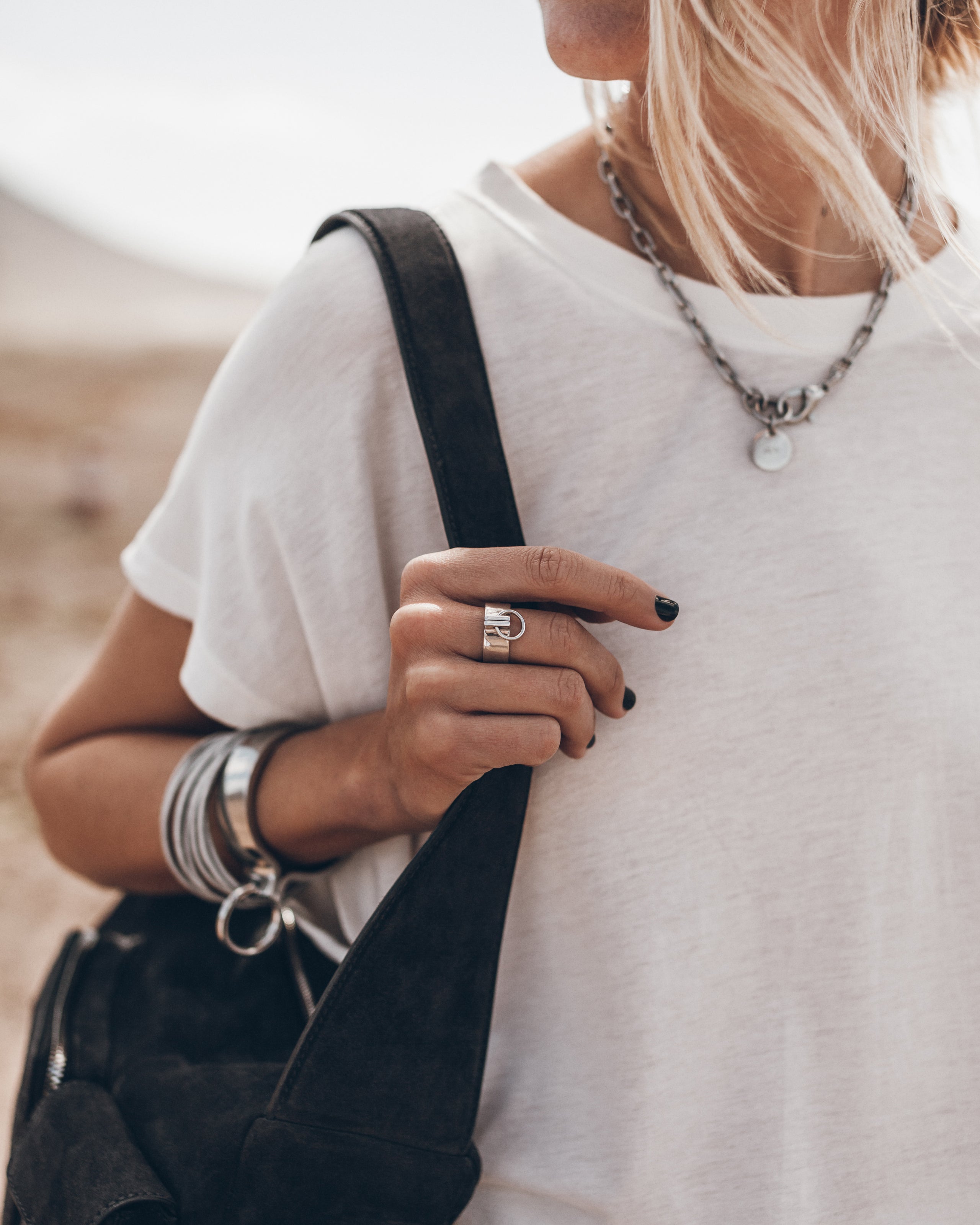 Person wearing a white t-shirt, black bag, and multiple necklaces with a blurred background