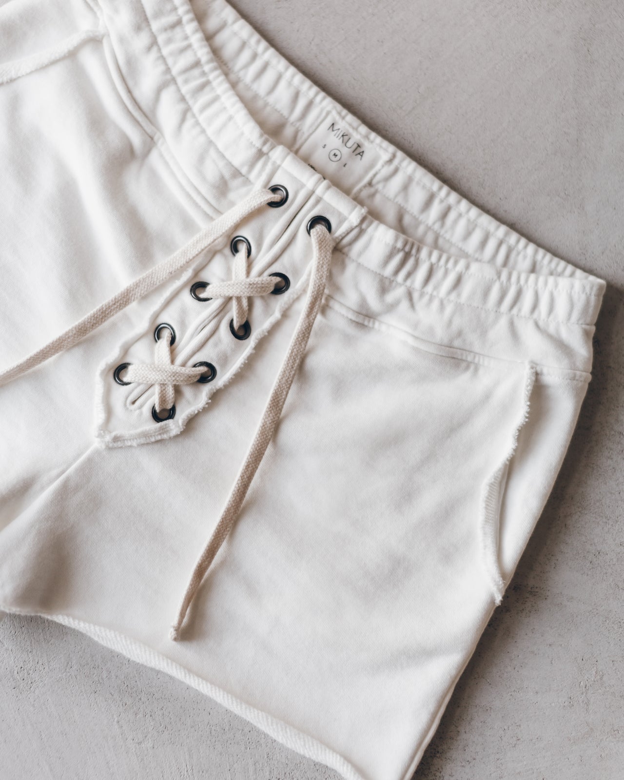 Ecru shorts with elastic waistband and front lace-up detail on soft fabric.