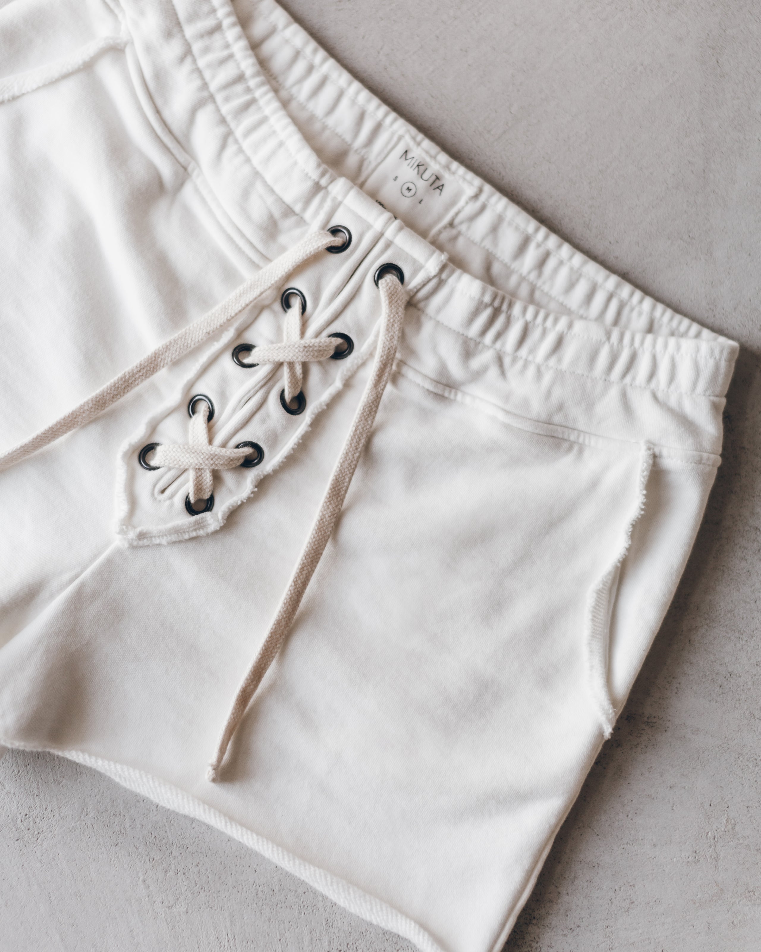 Ecru shorts with elastic waistband and front lace-up detail on soft fabric.