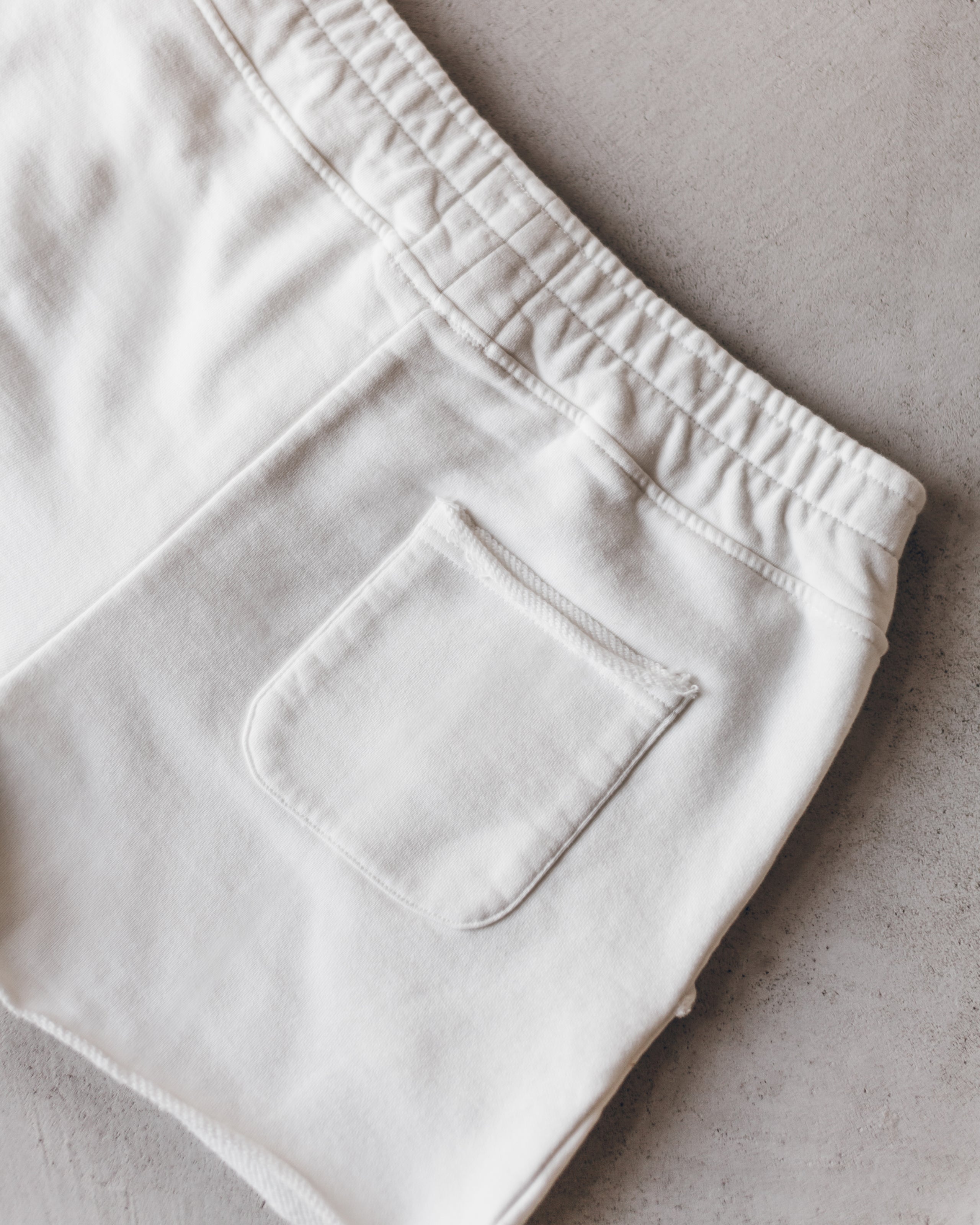 Ecru-colored shorts with elastic waistband and a single back patch pocket, soft fabric texture.