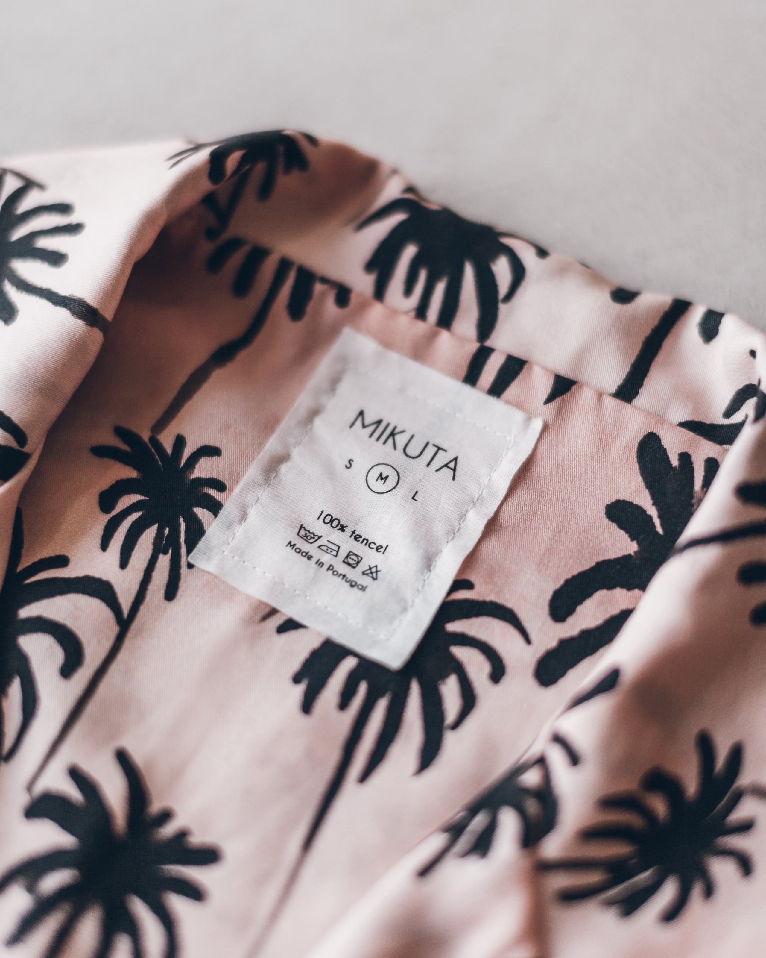 Light pink shirt with black palm tree print and Mikuta brand label inside neckline.