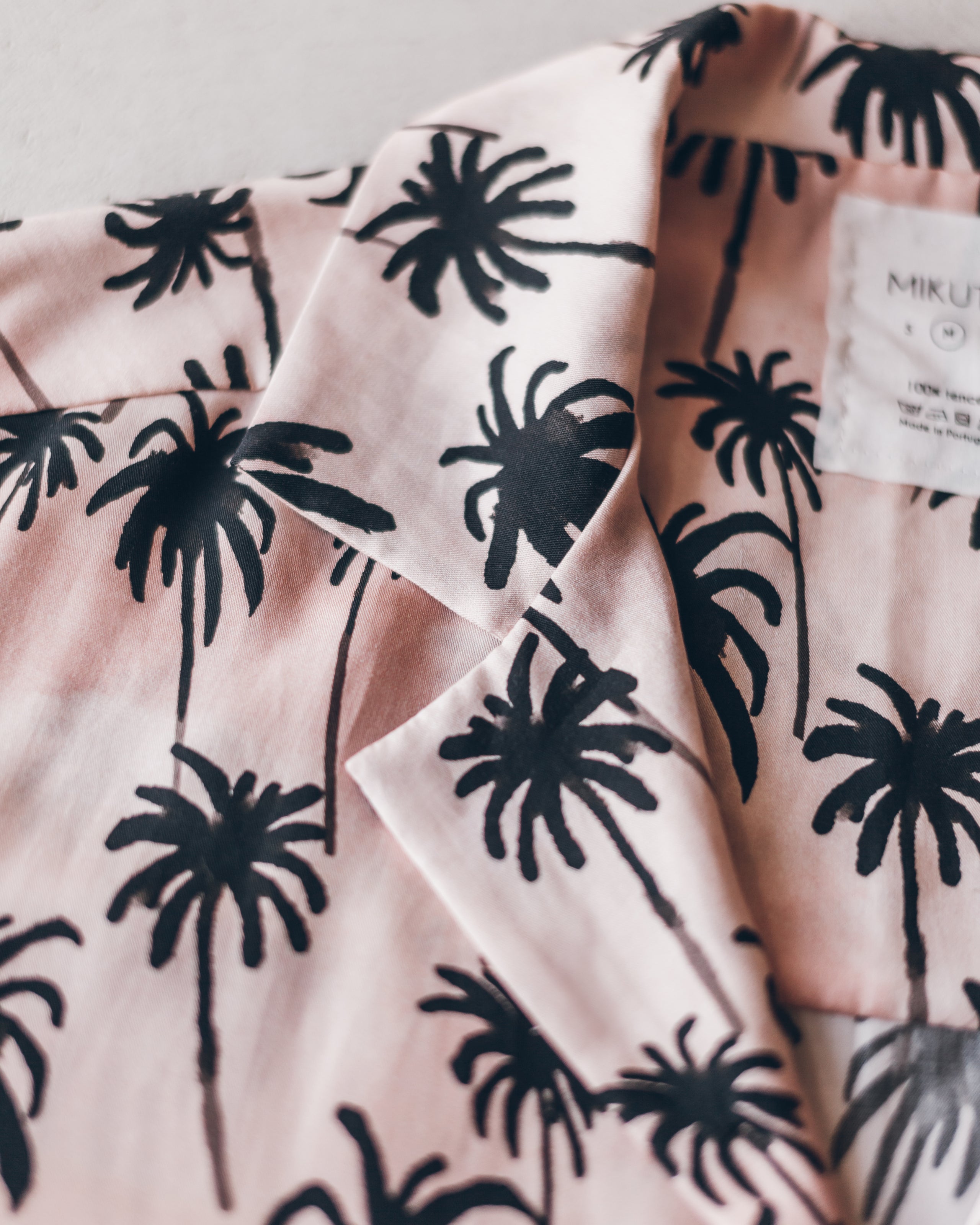 Light pink shirt with black palm tree print and classic collar detail.