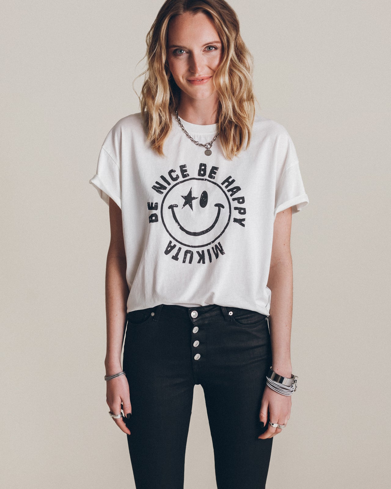 White relaxed-fit T-shirt with rolled sleeves and a black smiley face graphic that reads "Be Nice Be Happy Muktia".