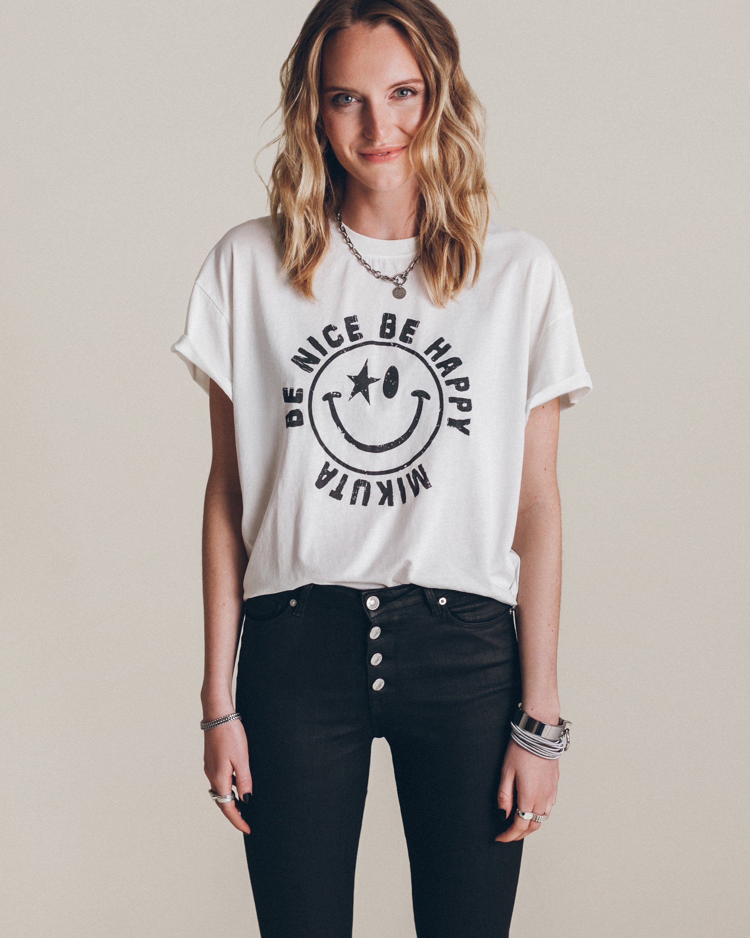White relaxed-fit T-shirt with rolled sleeves and a black smiley face graphic that reads "Be Nice Be Happy Muktia".