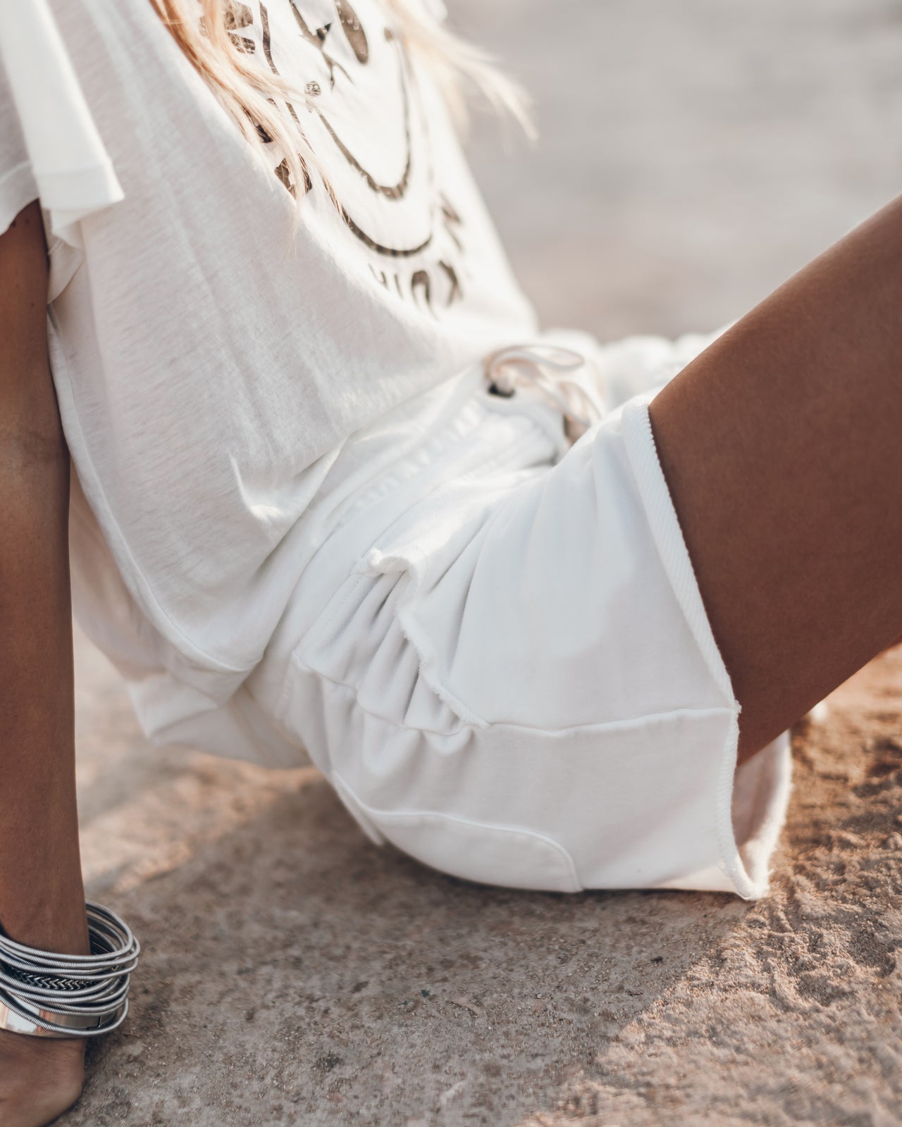 Ecru high-waisted shorts with a drawstring waist on a seated model wearing a white embroidered top.