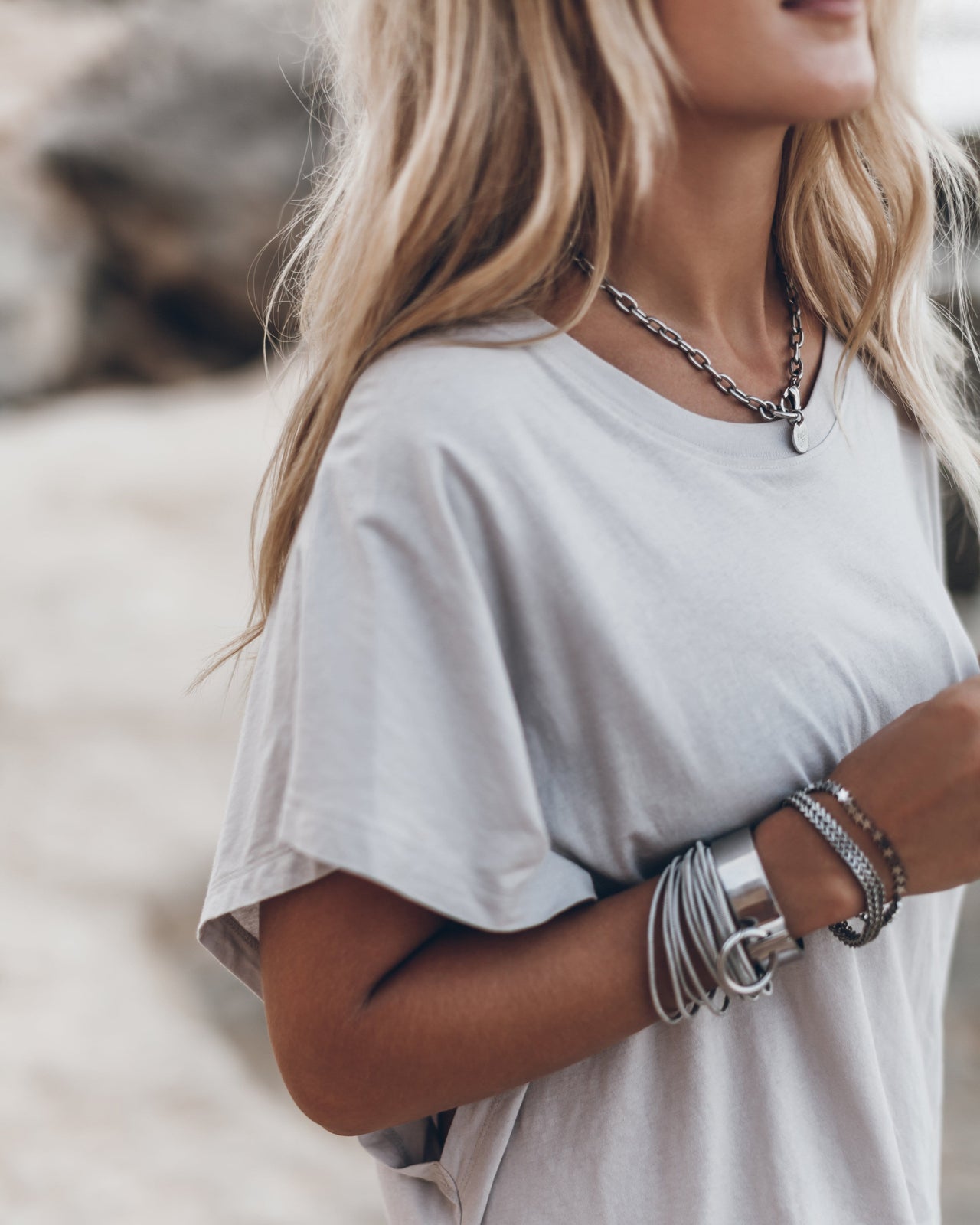 Light gray short-sleeve cotton T-shirt with a relaxed fit, worn with silver chain necklace and bracelets.