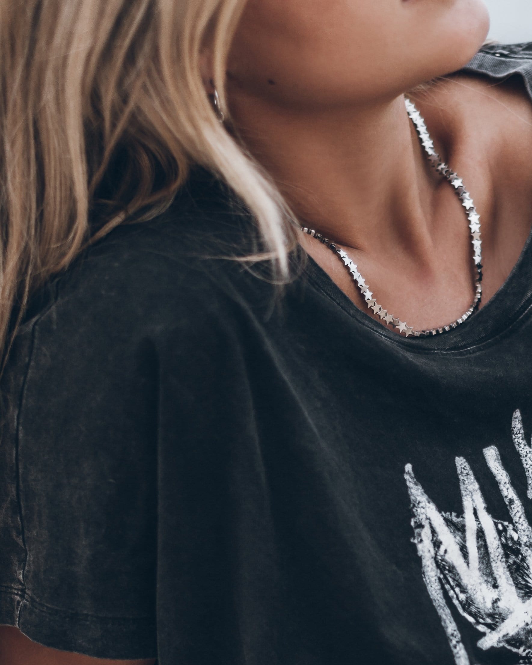 Close-up of black faded cotton T-shirt with white distressed print on front, worn with silver necklace.