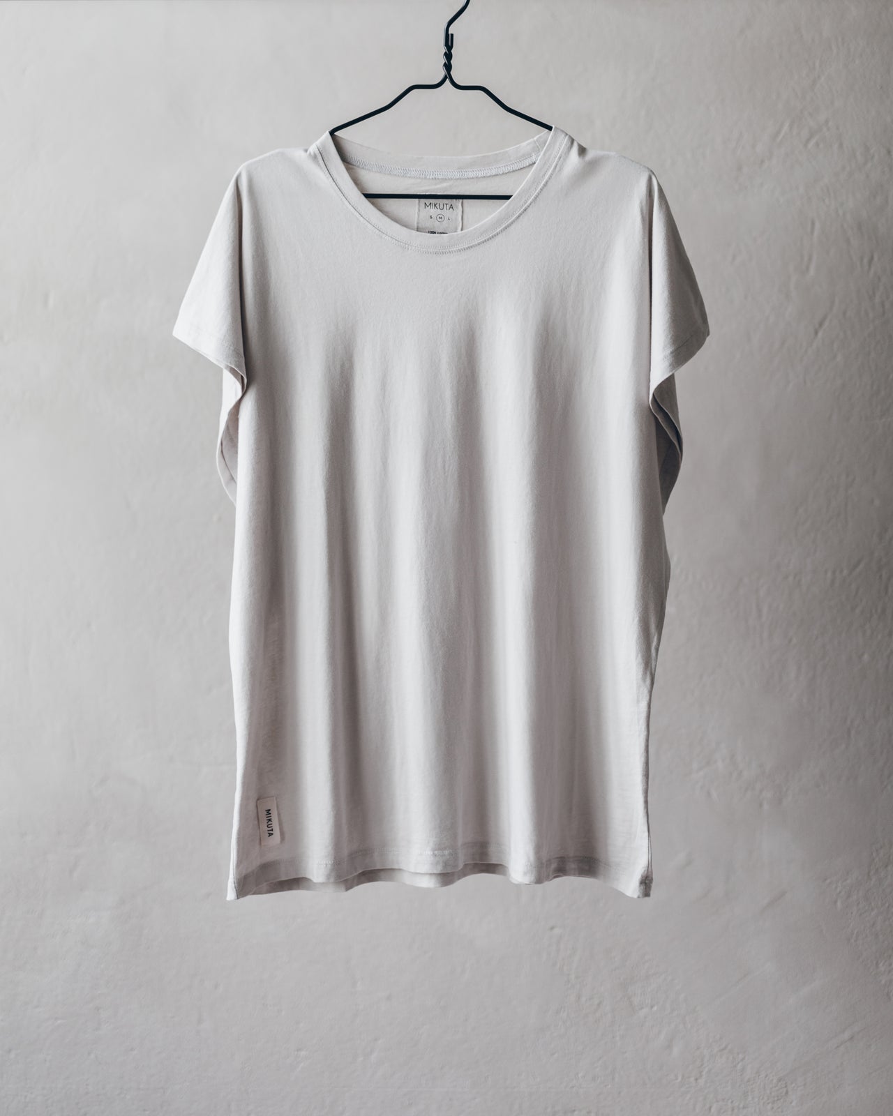Light gray short-sleeve crew neck t-shirt with relaxed fit hanging on black hanger.