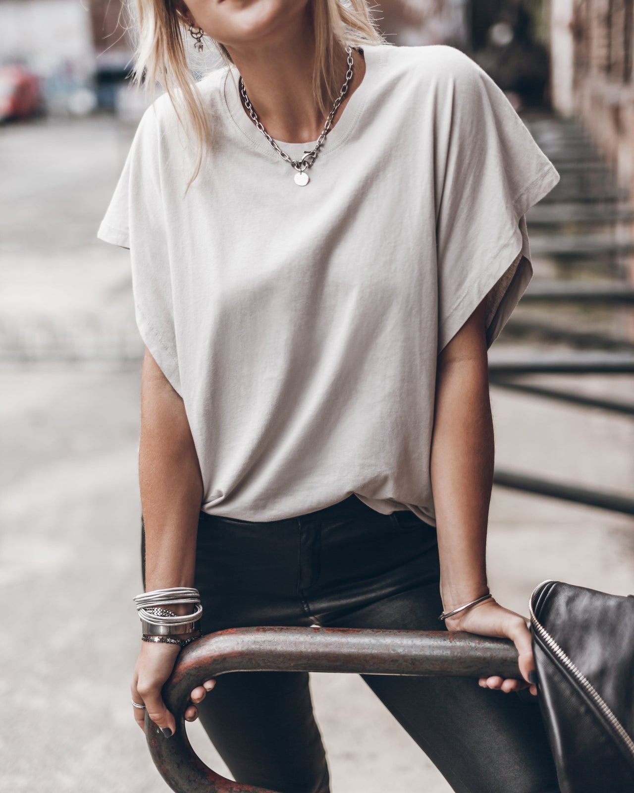 Soft white oversized T-shirt with rolled sleeves worn tucked into dark pants and layered necklaces.